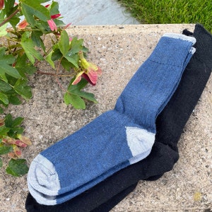 May include: Two pairs of socks, one blue and one black, are neatly arranged. The blue socks have gray accents on the toe and cuff. The black socks are solid. The socks are made of a soft, textured material.