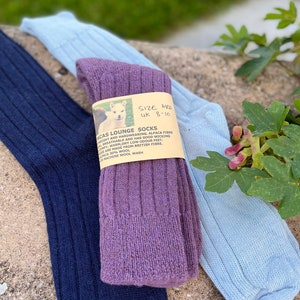 May include: Three pairs of ribbed knit socks in shades of navy blue, light blue, and purple. The purple pair has a label that reads "ALPACAS LOUNGE SOCKS" and "SIZE MED UK 8-10". The socks are made from British fiber.
