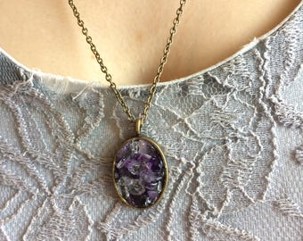 May include: A silver chain necklace with an oval pendant filled with small purple and clear amethyst crystals.