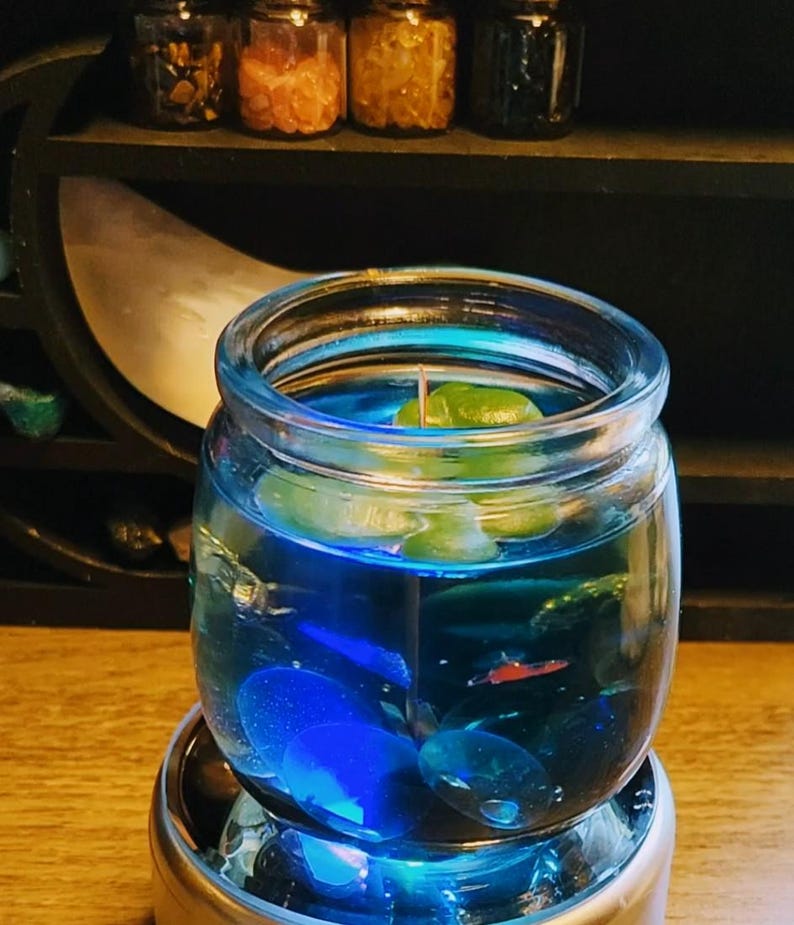 May include: A blue glass jar candle with teal wax and a white wick. The candle is sitting on a silver base and has blue and red glitter inside.