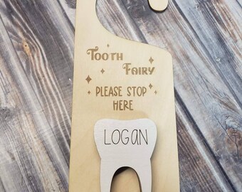 May include: Wooden tooth fairy door hanger with a tooth cutout and the name "Logan" inscribed. The hanger has the text "Tooth Fairy Please Stop Here" on it.