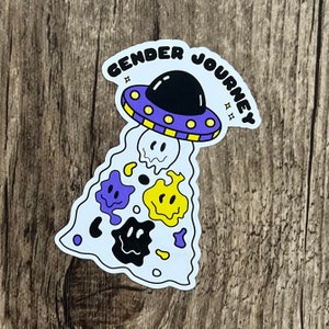 May include: A sticker featuring a cartoon UFO in purple, yellow and black. The text "Gender Journey" is above the UFO, which is emitting a stream of colourful, dripping smiley faces.