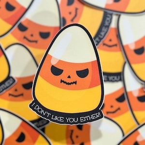May include: A Halloween-themed candy corn sticker with a grumpy face and the text "I don't like you either!"