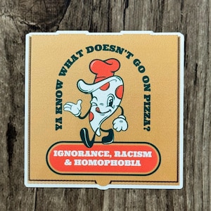 May include: A sticker featuring a cartoon pizza slice winking and gesturing. The pizza slice wears a chef's hat and has red and white toppings. Text on the sticker reads "YA KNOW WHAT DOESN'T GO ON PIZZA?" and "IGNORANCE, RACISM & HOMOPHOBIA."