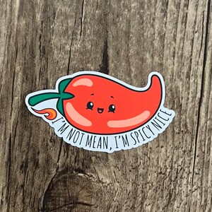 May include: A red chili pepper sticker with a smiling face and a small flame. The sticker has the text "I'M NOT MEAN, I'M SPICY NICE" in a white font. The chili pepper has a green stem.
