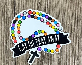 May include: A sticker featuring a rainbow coloured rosary and a black banner with the text "Gay the Pray Away".