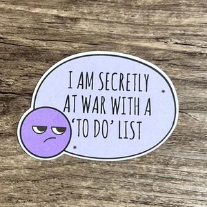May include: Purple sticker with a cartoon face and the text "I am secretly at war with a 'to do' list".