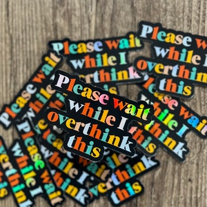 May include: A stack of black stickers with the text "Please wait while I overthink this" in colorful letters. The stickers are arranged in a random pattern.