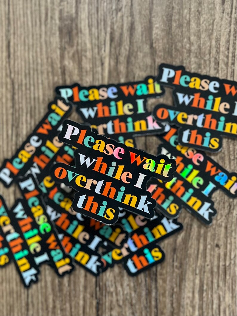 May include: A stack of black stickers with the text "Please wait while I overthink this" in colorful letters. The stickers are arranged in a random pattern.