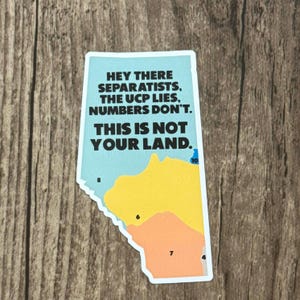 May include: A sticker in the shape of Alberta, Canada, with a light blue background and a map of the province in yellow and orange. The sticker has the text "HEY THERE SEPARATISTS, THE UCP LIES, NUMBERS DON'T. THIS IS NOT YOUR LAND."