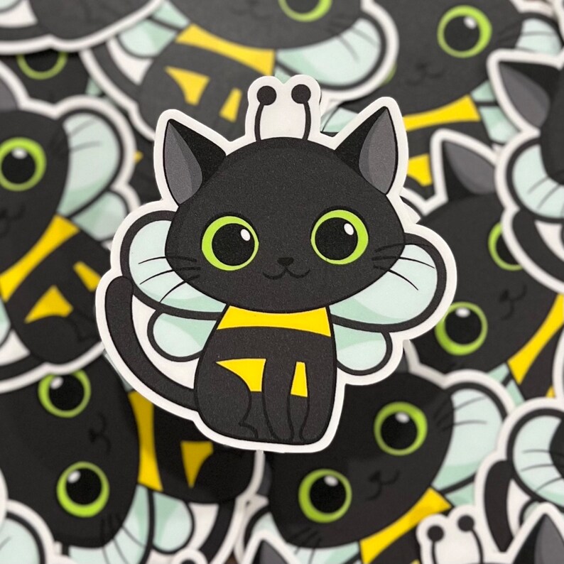 Peut inclure: Un chat noir avec des ailes d'abeille jaunes et noires. Le chat porte un costume d'abeille jaune et noir. Le chat a de grands yeux verts ronds.