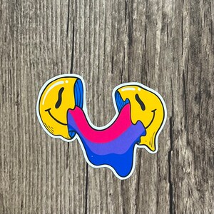 May include: Two yellow smiley faces with a blue and pink dripping paint design. The paint is in the colours of the bisexual pride flag.