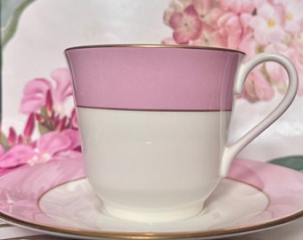 May include: A pink and white teacup and saucer with a gold trim. The cup has a pink band around the top and a gold band around the bottom. The saucer has a pink band around the edge and a gold band around the bottom.