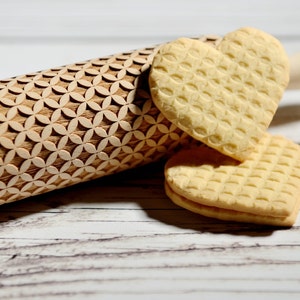 May include: A wooden rolling pin with a geometric pattern and two heart-shaped biscuits. The biscuits are light yellow and have a waffle-like texture.