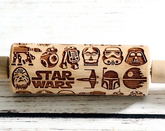 May include: A wooden rolling pin with a Star Wars theme. The rolling pin is engraved with images of characters and spaceships from the Star Wars movies, including Darth Vader, R2-D2, and the Millennium Falcon. The text "STAR WARS" is also engraved on the rolling pin.