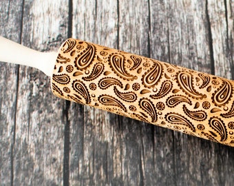 May include: A wooden rolling pin with a white handle and a paisley pattern carved into the surface.