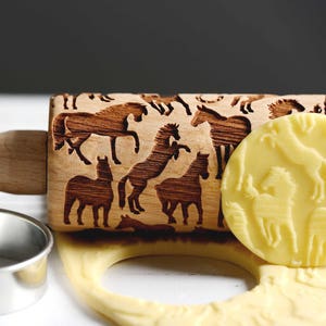 May include: A wooden rolling pin with a carved design of horses. The rolling pin is used to create decorative patterns on baked goods. A close-up of the rolling pin shows a detailed design of horses in a variety of poses.