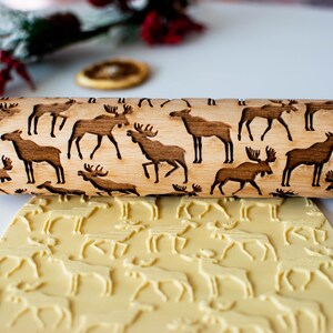 May include: A wooden rolling pin with a brown moose design engraved on the surface. The rolling pin is used to create decorative patterns in dough.