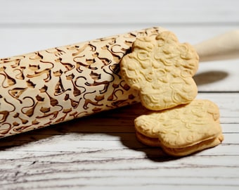 May include: A wooden rolling pin with a cat design engraved into the surface. Two cookies with the same cat design are next to the rolling pin.