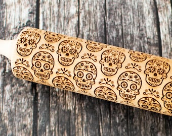 May include: A wooden rolling pin with a carved design of sugar skulls, a traditional Mexican motif. The skulls are decorated with flowers and other intricate details.