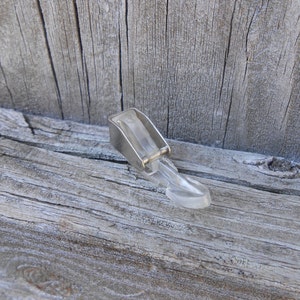 May include: A clear, plastic sewing machine foot with a silver metal attachment. The foot is designed to attach to a sewing machine and guide fabric during stitching. The foot is designed for sewing projects.