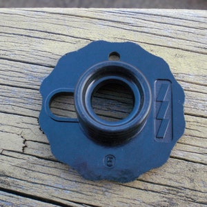 May include: A dark blue, plastic, circular object with a central hole and a smaller, curved opening. It features a raised, rectangular design with three angled lines and the number "(5)".