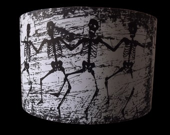 May include: A black and white lampshade with a design of four skeletons dancing on a distressed background.