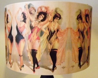 May include: A vintage lampshade with a colorful design featuring six women in various poses. The women are wearing costumes with feathers and fringe. The lampshade is made of fabric and has a white background.