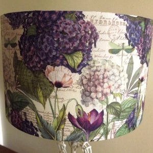 May include: A lampshade with a floral print featuring purple, white, and green flowers. The background is a cream colour with handwritten text.