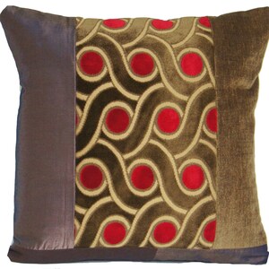 May include: A decorative throw pillow with a brown, beige, and red geometric pattern. The pillow has a brown velvet border.