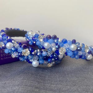 May include: Two blue and white beaded headbands with pearls. The headbands are made of small blue and white beads, with larger white pearls interspersed throughout.