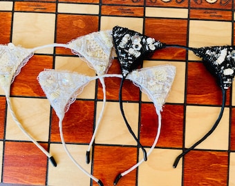 May include: Four cat ear headbands with white and black lace and beaded embellishments. Two headbands are white with white beads and two are black with white beads.