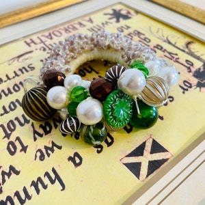 May include: A handmade beaded wreath with brown, white, and green beads. The wreath is made with a variety of beads, including pearls, glass beads, and wooden beads.