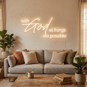 May include: A wall-mounted neon sign featuring the illuminated white text "with God all things are possible" in a combination of cursive and sans-serif fonts. The sign emits a warm glow against the wall, positioned above a gray sofa with pillows.