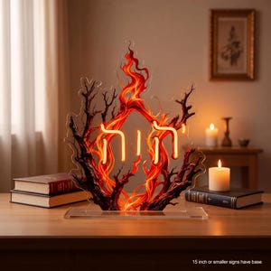May include: A decorative acrylic sign featuring a bright orange neon Hebrew inscription centred within a stylised flame and dark branch design. The sign is mounted on a clear rectangular base and includes text stating that 15 inch or smaller signs have a base.