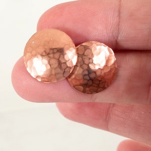 May include: A pair of round, hammered copper earrings. The earrings are a light copper color and have a textured surface.