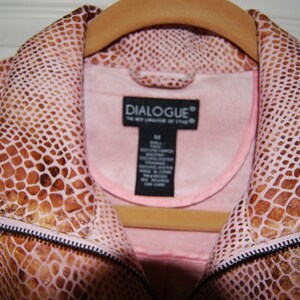 May include: A pink snakeskin jacket with a brown snakeskin pattern. The jacket has a zipper closure and a collar. The label on the jacket reads "DIALOGUE&reg; The New Language of Style".