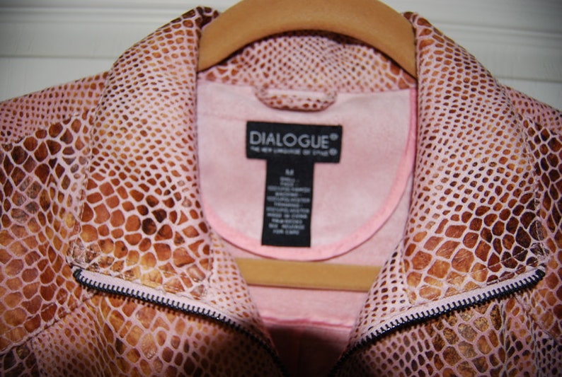 May include: A pink snakeskin jacket with a brown snakeskin pattern. The jacket has a zipper closure and a collar. The label on the jacket reads "DIALOGUE&reg; The New Language of Style".
