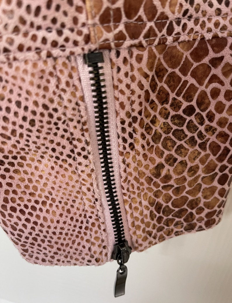 May include: Close-up of a pink and brown snakeskin-patterned fabric with a black zipper. The zipper is partially open and the zipper pull is visible.