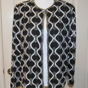 May include: A black and white sequined jacket with a geometric pattern. The jacket has a long sleeve and a front closure.