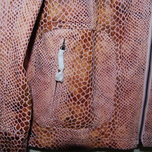 May include: Close-up of a pink and brown snakeskin jacket with a zipper closure and a pocket on the left side.