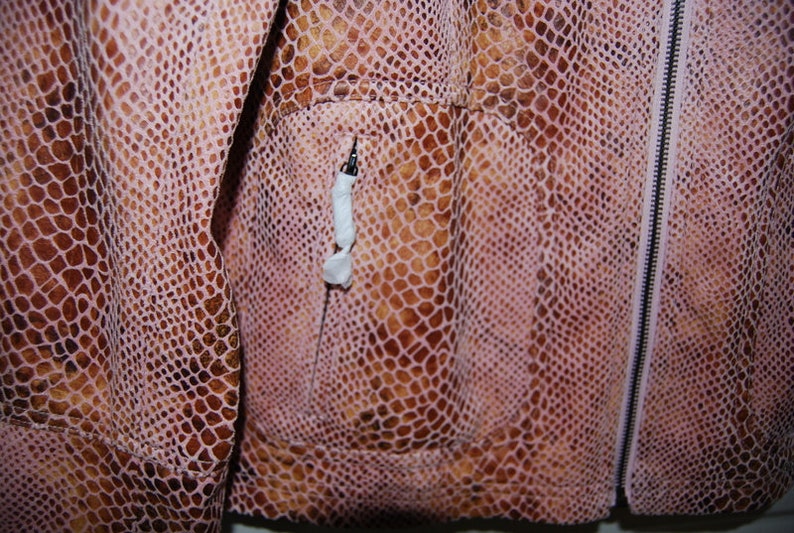 May include: Close-up of a pink and brown snakeskin jacket with a zipper closure and a pocket on the left side.