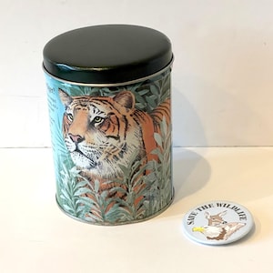 May include: A cylindrical tin with a black lid and a detailed illustration of a tiger in a jungle setting. A small, round button with the text "SAVE THE WILDLIFE" and a wildlife graphic is next to the tin.