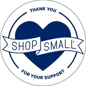May include: A white circle with a blue heart in the center. The heart has a white banner that says "SHOP SMALL" with a registered trademark symbol. The circle also has the text "THANK YOU" at the top and "FOR YOUR SUPPORT" at the bottom.
