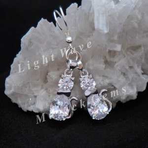 May include: Silver dangle earrings featuring a pair of cats with clear cubic zirconia stones. The cats are facing each other and have a tail.
