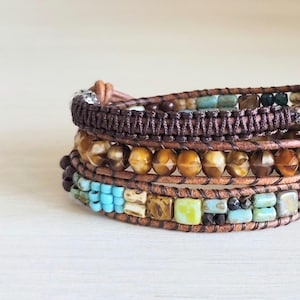 Op de afbeelding: Een meerstrengs wikkelarmband met bruine leren koorden, gefacetteerde barnsteenkleurige kralen, donkerbruine gevlochten koordsecties en diverse kleine vierkante en rechthoekige kralen in tinten turquoise, limoengroen en gevlekt bruin.