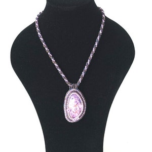 May include: A purple beaded necklace with a large, oval-shaped pendant. The pendant is made of purple beads and has a textured, iridescent finish.