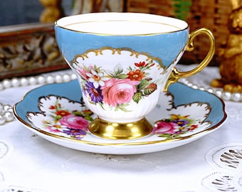 May include: A vintage teacup and saucer set with a blue and white floral design. The cup has a gold rim and a delicate floral pattern. The saucer has a matching floral design and a scalloped edge.