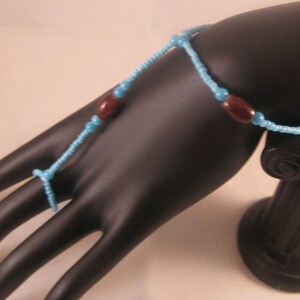 May include: A turquoise and brown beaded bracelet with a ring attached. The bracelet is made of small beads and has two brown accent beads.