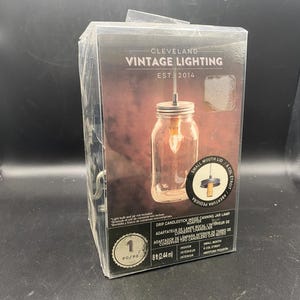 Könnte beinhalten: Eine verpackte Cleveland Vintage Lighting Einmachglaslampe. Die Verpackung zeigt ein Foto der Lampe, ein Glas mit kleinem Munddeckel und einer Hängeleuchte. Die Box enthält auch den Text "EST. 2014".